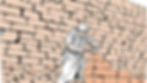 A man in white laying bricks. In the background we see a huge wall that he has built over time.