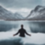 Man in black jacket sits on snowy edge of a calm lake, surrounded by snow-covered mountains under a cloudy sky, evoking tranquility.