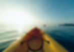 Yellow kayak in calm water at sunrise, with other kayakers in the distance. Sky is clear, creating a serene, peaceful mood.